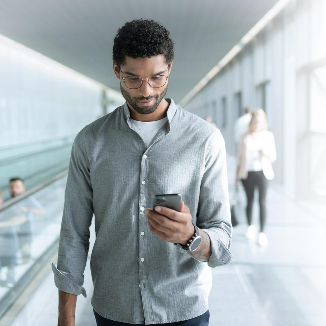 Egy ZEISS SmartLife szemüveglencsét viselő fiatalember nézi a telefonját séta közben.