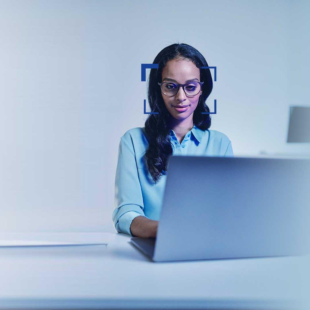Fekete hajú, szemüveges nő mosolyogva néz egy laptopra