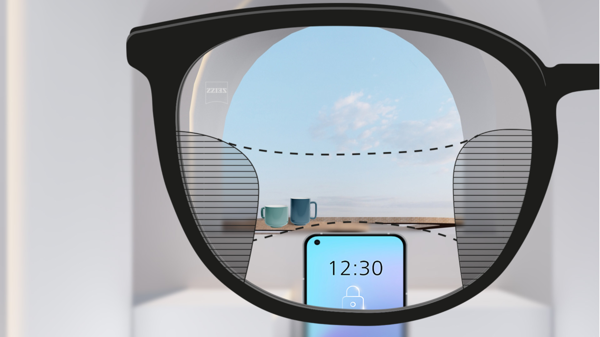 Személyes nézőpontból készült kép egy ZEISS SmartLife progresszív szemüveglencséről, amelyen keresztül élesen látszik a háttérben egy okostelefon és két bögre; a lencse bal és jobb oldalán pedig apró homályos részek látszanak.