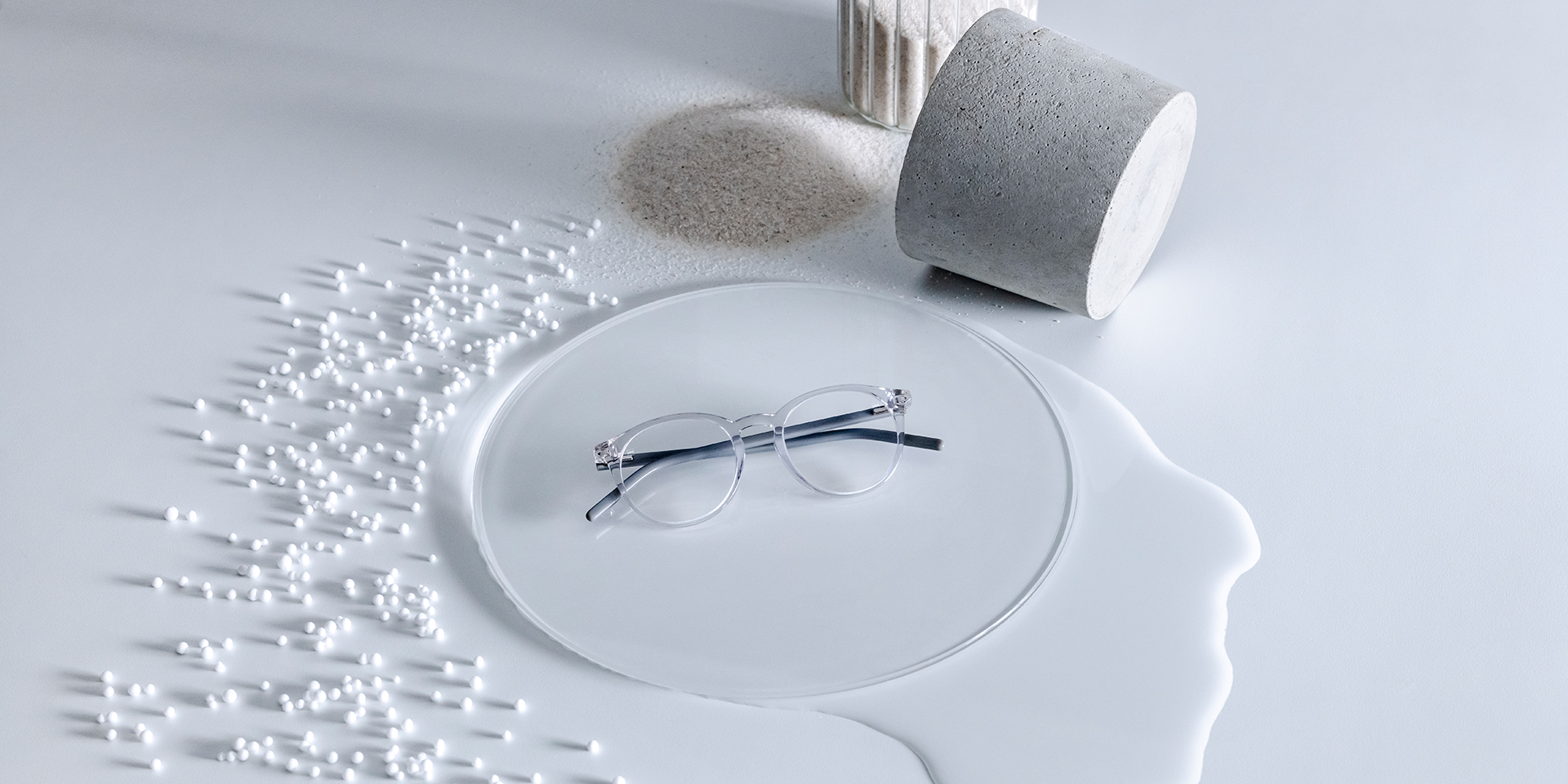 DuraVision® felületkezeléssel ellátott ZEISS lencsék egy üvegből készült talapzaton, amelyet víz, homok, gyöngyök és kövek vesznek körben.
