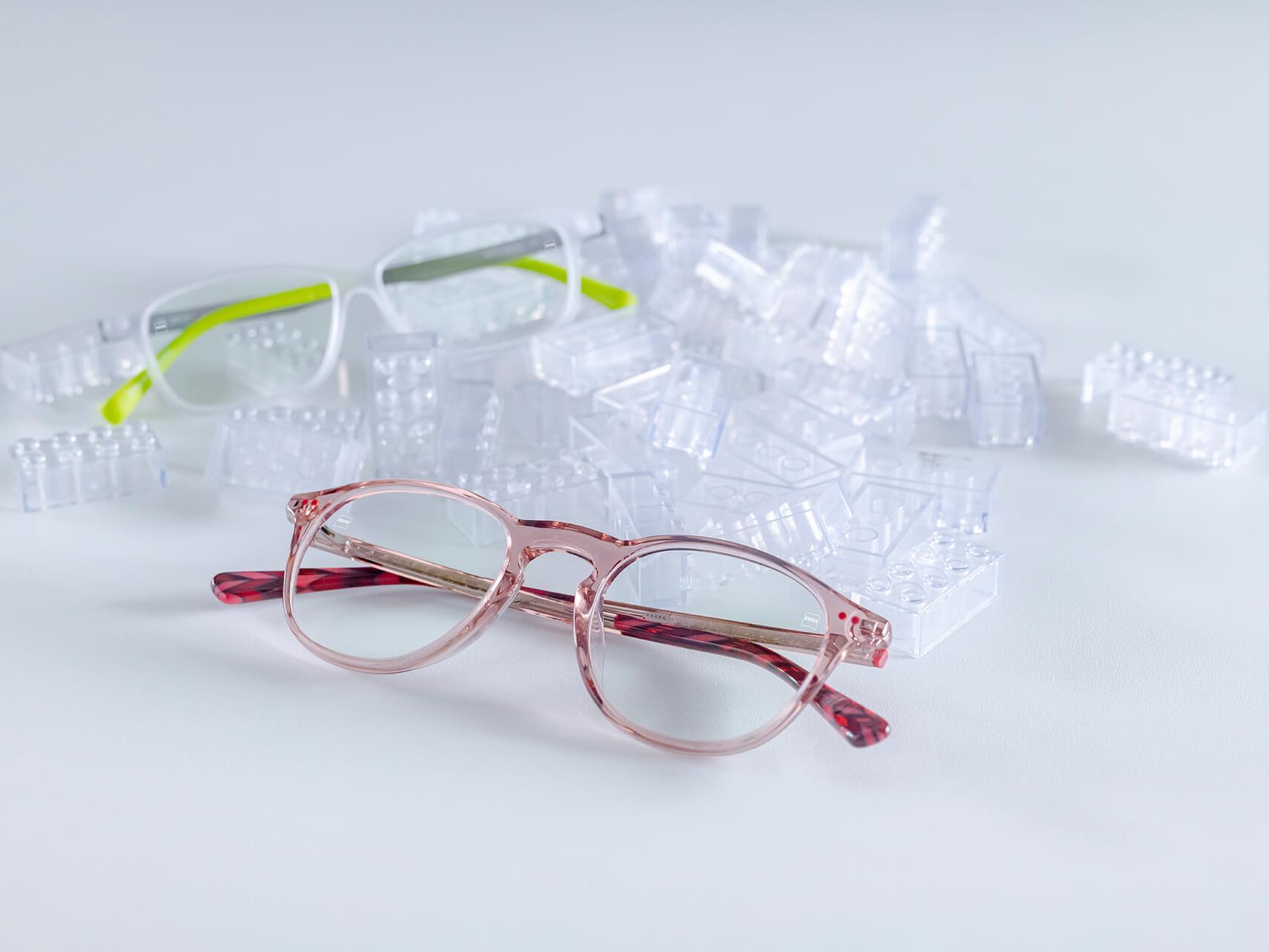 Két gyermekszemüveg ZEISS lencsékkel, amelyek DuraVision® Kids felületkezelésekkel vannak ellátva. A szemüvegek átlátszó építőkockák közé vannak helyezve.