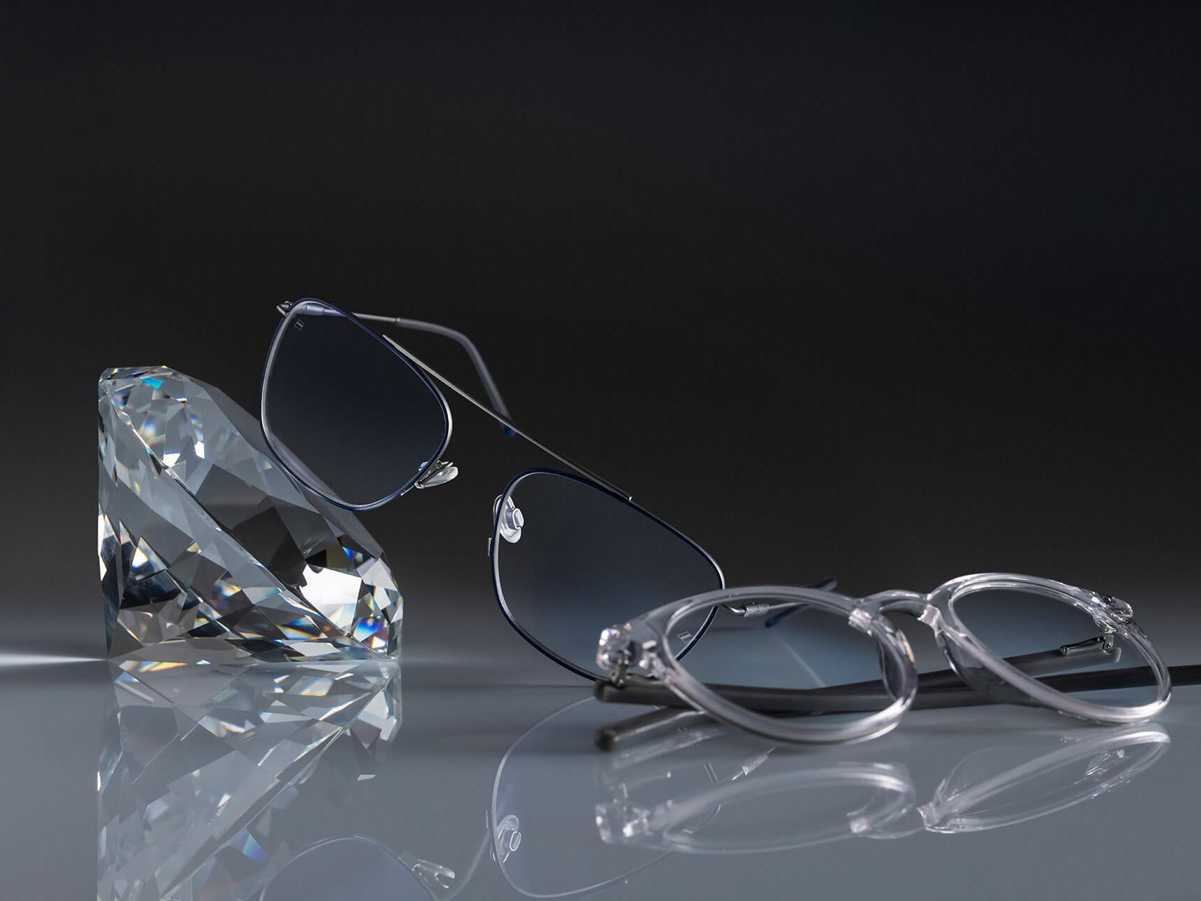 Két szemüveg ZEISS lencsékkel, amelyek a legkeményebb ZEISS rétegezéssel vannak ellátva – a DuraVision® Platinum rétegezéssel. Az egyik szemüveg egy kristálynak van támasztva, a másik a földön van elhelyezve. Mindkettő lencséje teljesen átlátszó, kék tükröződések nélkül.