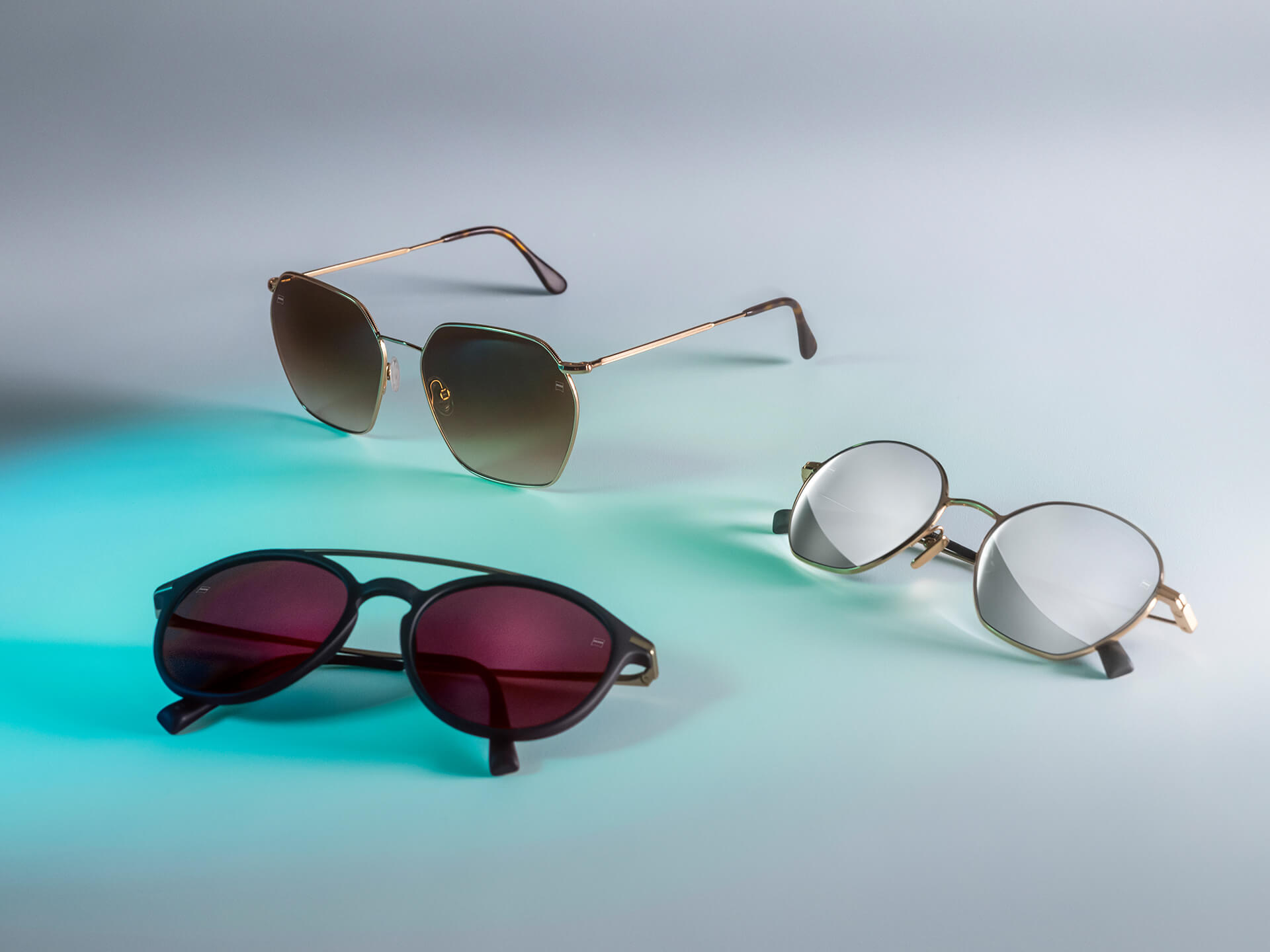 Három napszemüveg különböző színű ZEISS lencsékkel: DuraVision Sun, DuraVision Mirror és Flash tükrös hatású felületkezelésekkel; mindez fehér háttér előtt, kék fényű tükröződéssel.