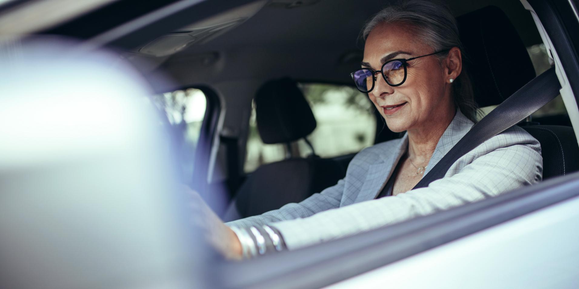 Autót vezető idős hölgy, aki ZEISS DriveSafe lencséjű szemüveget visel.