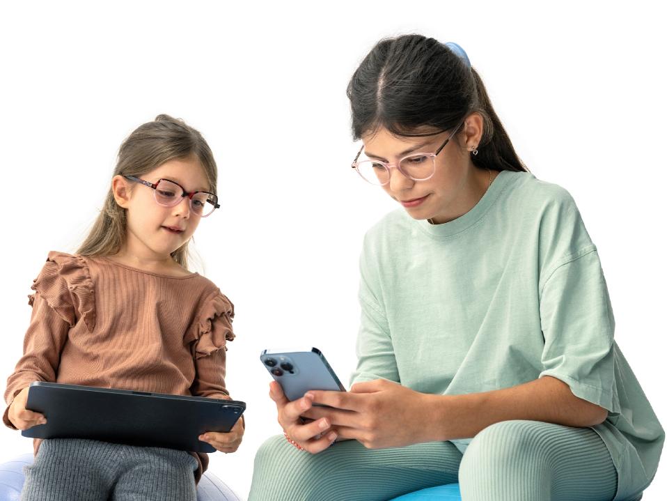 Két lány digitális eszközöket néz, az ajánlott 20 cm-es távolságnál nagyobb távolságból.