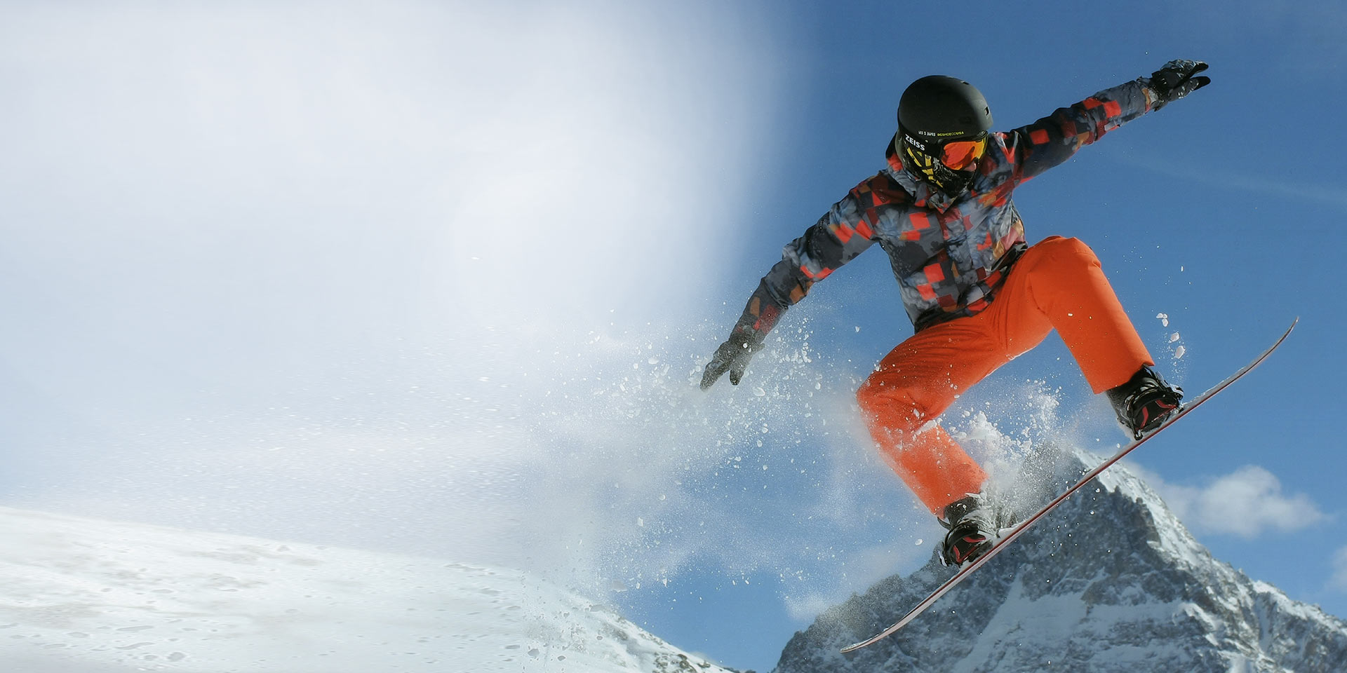 Egy férfi snowboarddal ugrik, fekete sisakot és ZEISS cserélhető lencsés technológiával ellátott síszemüveget visel a védelem érdekében