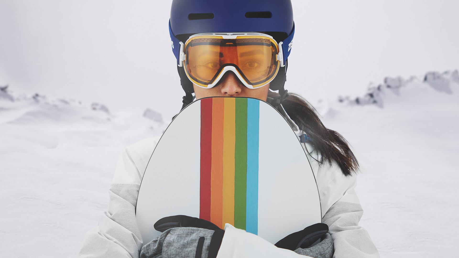 Snowboardot tartó és ZEISS cserélhető lencsés technológiával ellátott síszemüveget viselő fiatal nő.