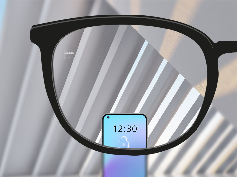 Saját szemszögből készült kép egy ZEISS SmartLife egyfókuszú szemüveglencséről, amelyen keresztül élesen látszik egy okostelefon és a szemüveglencse többi része. 