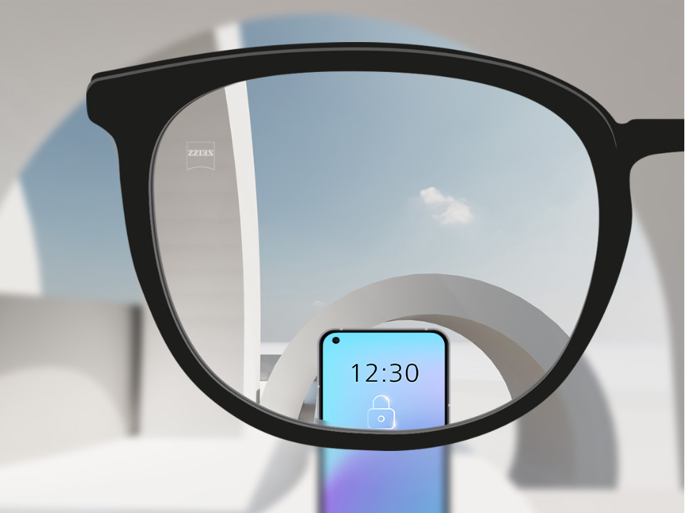 Saját szemszögből készült kép egy ZEISS SmartLife egyfókuszú szemüveglencséről, amelyen keresztül élesen látszik egy okostelefon és a szemüveglencse többi része.