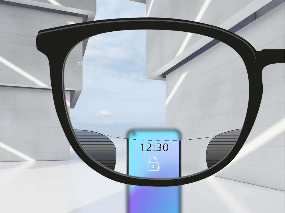 Saját szemszögből készült kép egy ZEISS Digital SmartLife szemüveglencséről, amelyen keresztül élesen látszik az okostelefon, valamint a lencse felső és alsó része; a lencse bal és jobb oldalán pedig apró homályos részek látszanak.