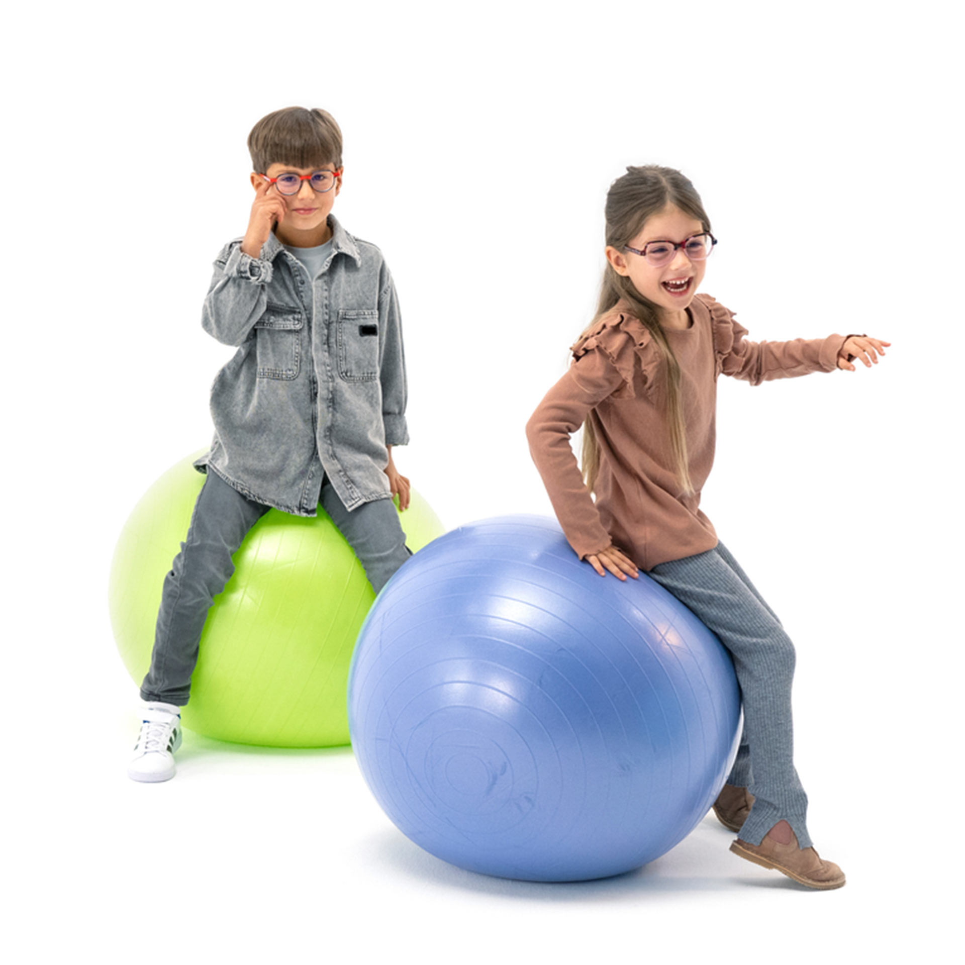 Szemüveget viselő kisfiú és kislány, amint játékosan ugrálnak gimnasztikai labdákon.